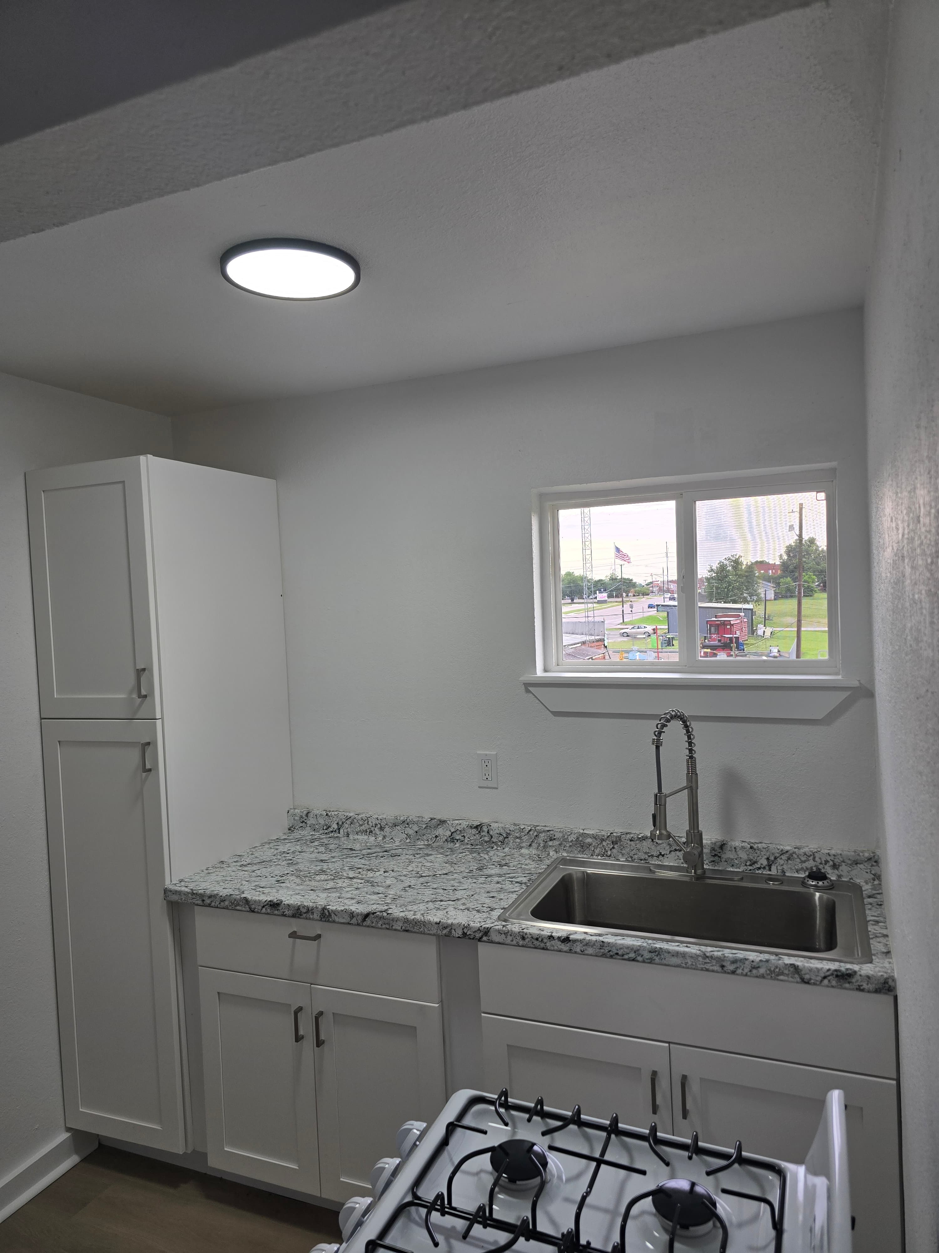 Renovated studio kitchen with white cabinets, stone-look counters, and gas range